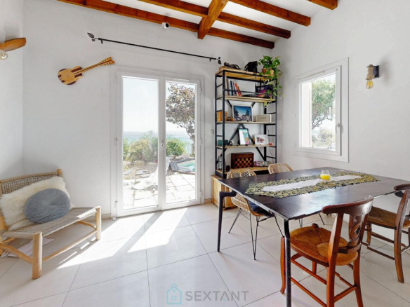 Intérieur d'une villa avec table à manger, étagères et fenêtres offrant une vue sur l'extérieur.