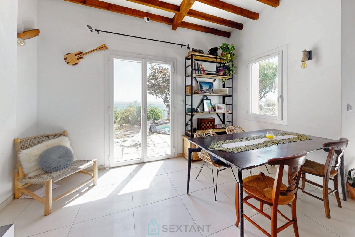 Intérieur d’une villa à Istres Intérieur d'une villa avec table à manger, étagères et fenêtres offrant une vue sur l'extérieur.