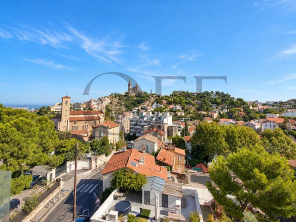 Vue panoramique sur Marseille avec Notre-Dame de la Garde en arrière-plan et des toits typiques au premier plan.