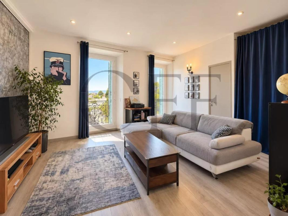 Salon lumineux d'un duplex avec canapé et télévision, fenêtres donnant sur une vue panoramique.