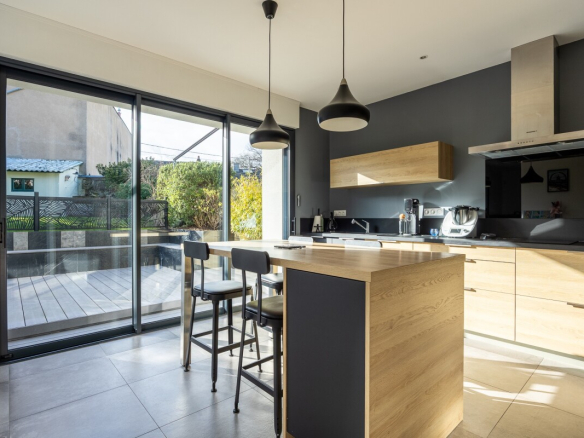 Modern kitchen with central island and large windows overlooking the outside.