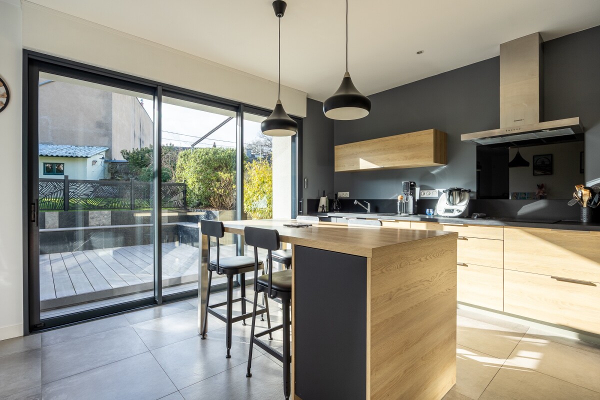 Modern kitchen with central island and large windows overlooking the outside.
