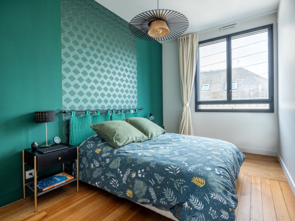 Bedroom in a house in Nantes with green walls and a bed decorated with cushions.