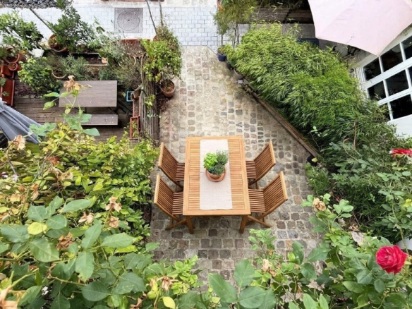 Terrasse en pierre avec table en bois et chaises, entourée de verdure et de plantes.