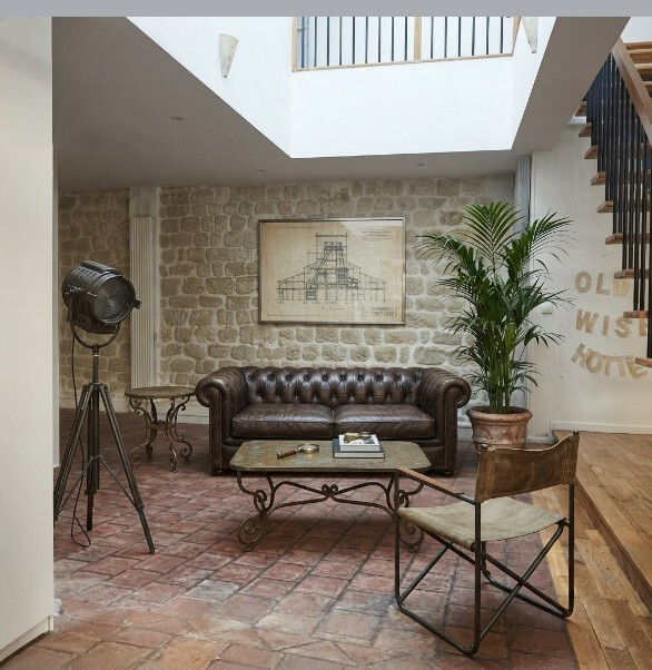 Intérieur d’une maison atypique à Paris Intérieur d'une maison atypique avec canapé en cuir, plante, et décor en pierre apparente.