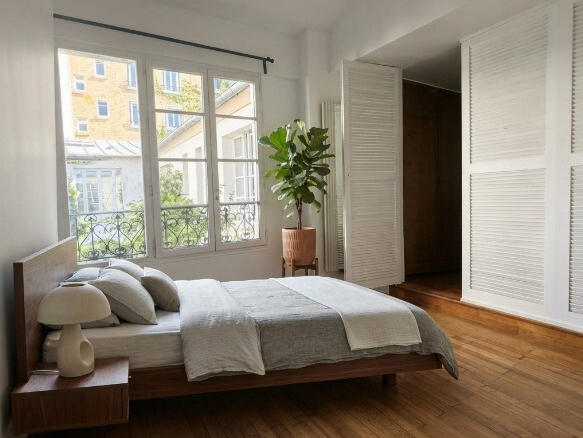 Chambre lumineuse avec lit, plantes et fenêtres à Paris 19ème.