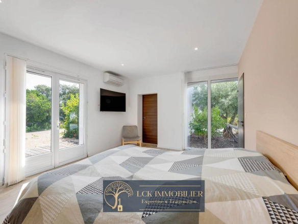 Chambre d'une villa contemporaine avec vue sur le jardin, lit double et fenêtres ouvertes sur l'extérieur.