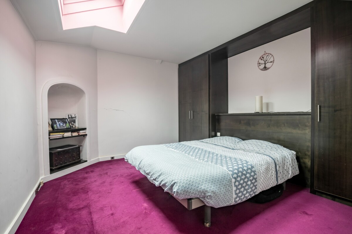 Chambre d’atelier d’artiste à Paris Chambre d'un atelier d'artiste avec un lit, moquette rose et lumière naturelle.