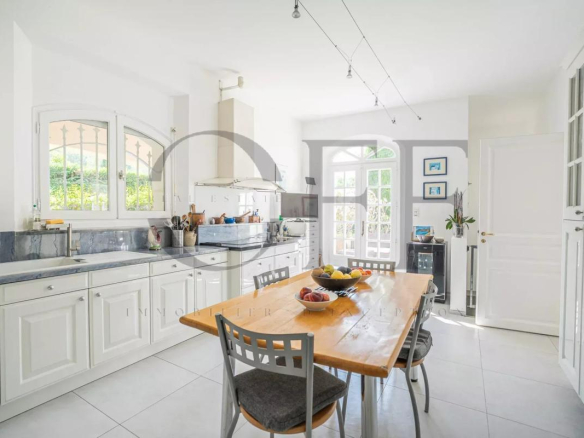 Cuisine lumineuse d'une villa d'exception à Marseille 12ᵉ avec table en bois et fenêtres ouvertes sur l'extérieur.