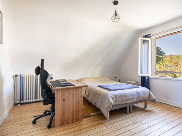 Chambre lumineuse avec un lit double, un bureau en bois et une fenêtre ouverte sur l'extérieur.
