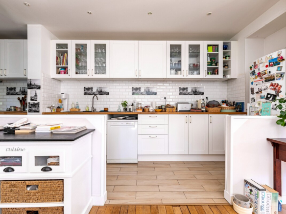 Cuisine moderne avec meubles blancs et carrelage clair, vue sur un plan de travail en bois.