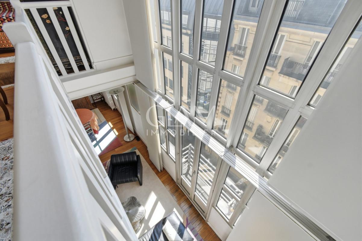 Intérieur d'un duplex avec grandes fenêtres et vue sur la Tour Eiffel à Paris.