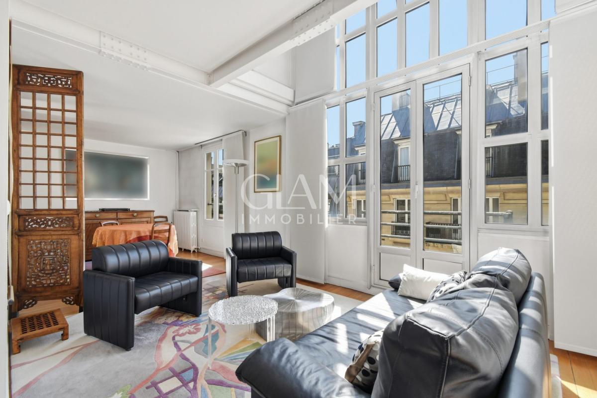 Intérieur d'un duplex lumineux avec vue sur la Tour Eiffel, salon moderne avec canapé et fauteuils.