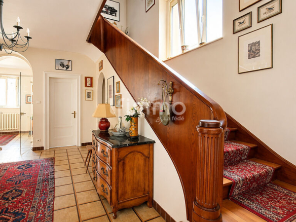 Intérieur d'une maison bourgeoise avec un escalier central en bois et des décorations murales.