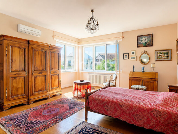 Chambre d'une maison bourgeoise à Barr, avec lit, armoire en bois et fenêtres lumineuses.
