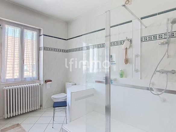 Salle de bain moderne avec baignoire et douche, carrelage blanc, fenêtre lumineuse.