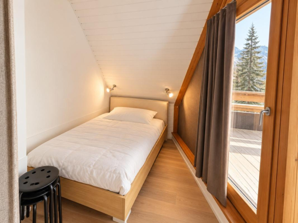 Chambre d'un appartement lumineux avec lit simple et vue sur les montagnes à Morzine.