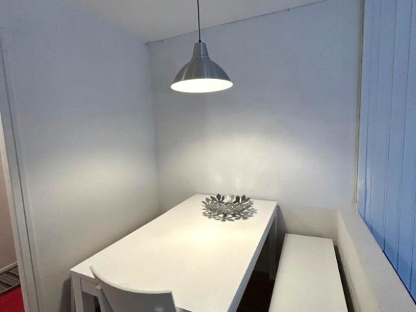 Salle à manger d'un appartement lumineux avec table blanche et banc, lumière suspendue.