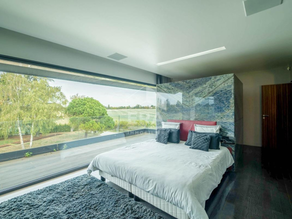 Chambre moderne avec grande fenêtre offrant une vue sur l'extérieur, décorée avec un lit et des textiles neutres.