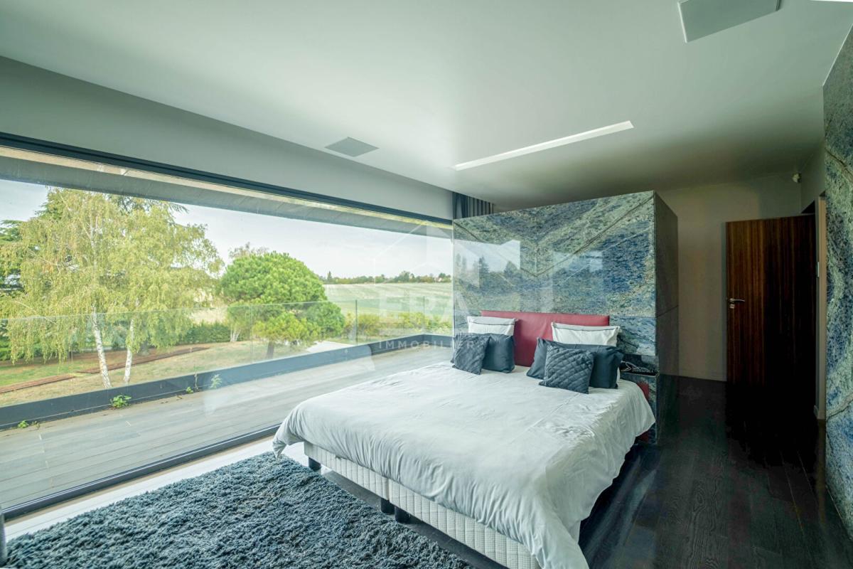 Chambre moderne avec grande fenêtre offrant une vue sur l'extérieur, décorée avec un lit et des textiles neutres.