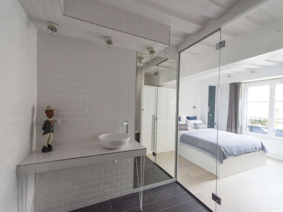 Salle de bain moderne avec lavabo et miroir, chambre à coucher lumineuse avec lit et fenêtres.