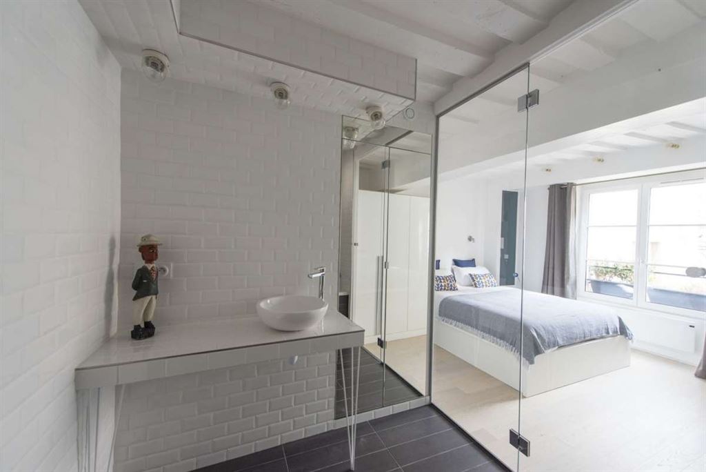 Bel appartement dans le Marais Salle de bain moderne avec lavabo et miroir, chambre à coucher lumineuse avec lit et fenêtres.