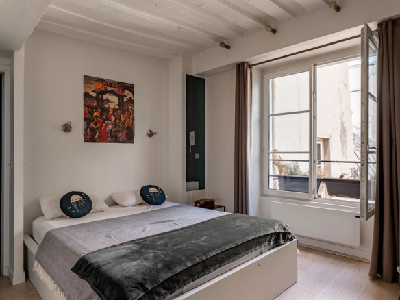 Chambre d'un appartement meublé au Marais, Paris, avec lit double et fenêtres ouvertes.