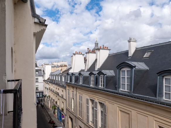 Vue des toits du Marais à Paris avec des bâtiments historiques et un ciel nuageux.