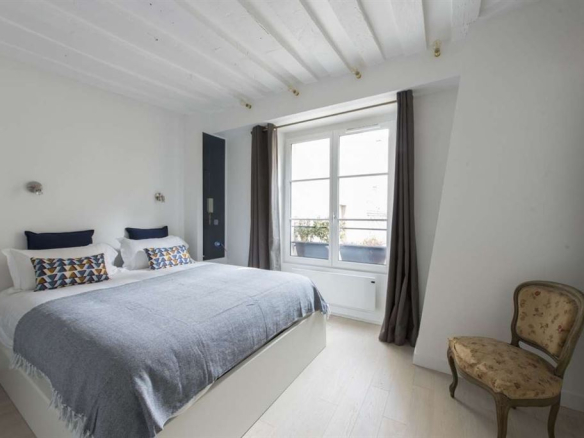 Chambre d'un appartement meublé au Marais, Paris, avec lit double et fenêtre.