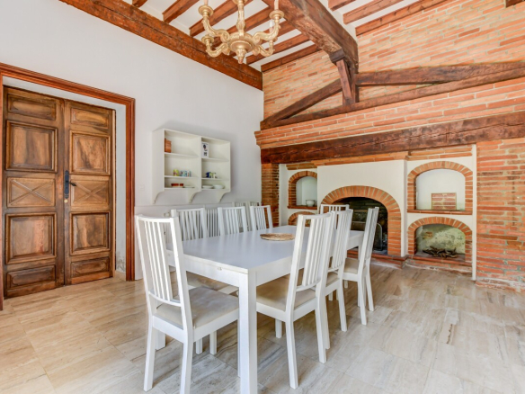 Salle à manger avec table blanche et chaises, cheminée en briques, murs en brique apparente.
