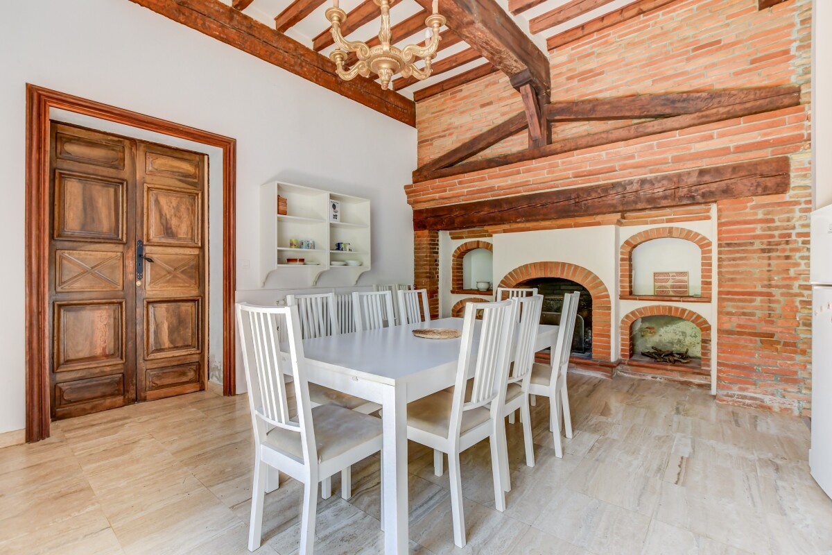Salle à manger du château à Lanta Salle à manger avec table blanche et chaises, cheminée en briques, murs en brique apparente.