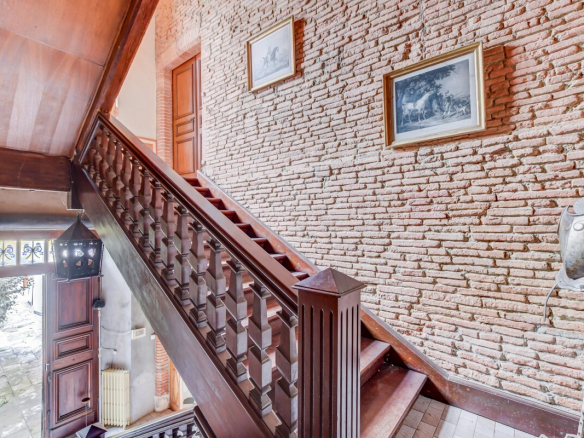 Escalier en bois dans un château du XVIIe siècle à Lanta, avec murs en briques apparentes.