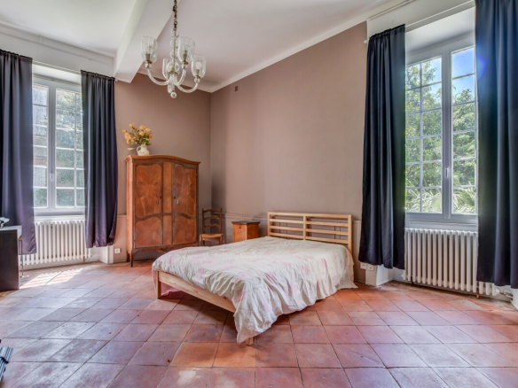Chambre d'un château du XVIIe siècle à Lanta avec un lit, une armoire en bois et des fenêtres lumineuses.