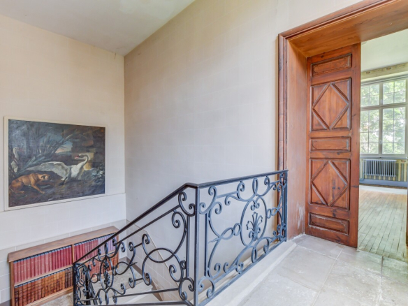 Escalier avec balustrade en fer forgé menant à un espace lumineux, avec une peinture accrochée au mur.