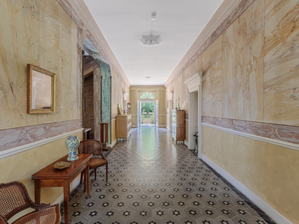 Intérieur d'une maison de maître du XIXe siècle avec un couloir large et décoré, sol en carreaux.
