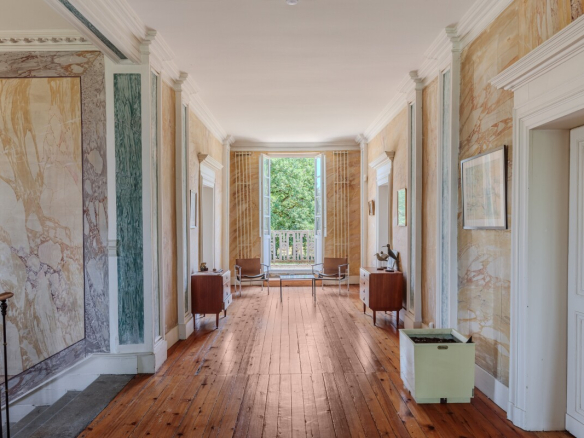 Intérieur d'une maison du XIXe siècle avec un couloir lumineux et des murs ornés de marbre.