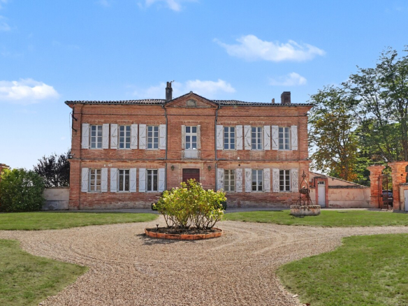 Maison de maître en briques au cœur d'un domaine, entourée d'un jardin paysagé.