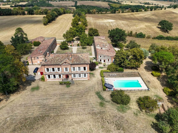Vue aérienne d'une propriété avec maison de maître, dépendances et piscine, entourée de champs.