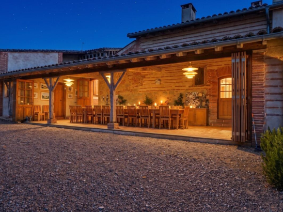 Terrasse d'une maison de maître avec des tables en bois, éclairage chaleureux, et murs en briques apparentes.