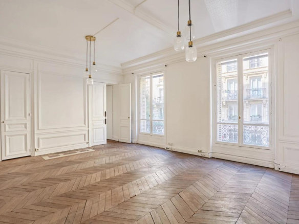Intérieur d'un appartement spacieux avec parquet en chevrons et grandes fenêtres à Paris.