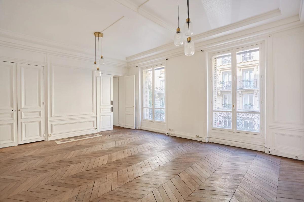 Appartement à rénover à Paris 8ème Intérieur d'un appartement spacieux avec parquet en chevrons et grandes fenêtres à Paris.
