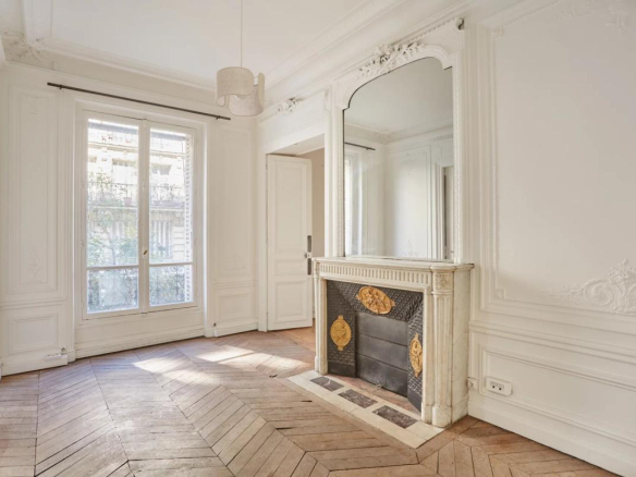 Intérieur d'un appartement à rénover avec parquet en point de Hongrie et cheminée en marbre.