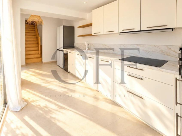 Intérieur d'une cuisine moderne avec des meubles clairs et un accès à un escalier en bois.