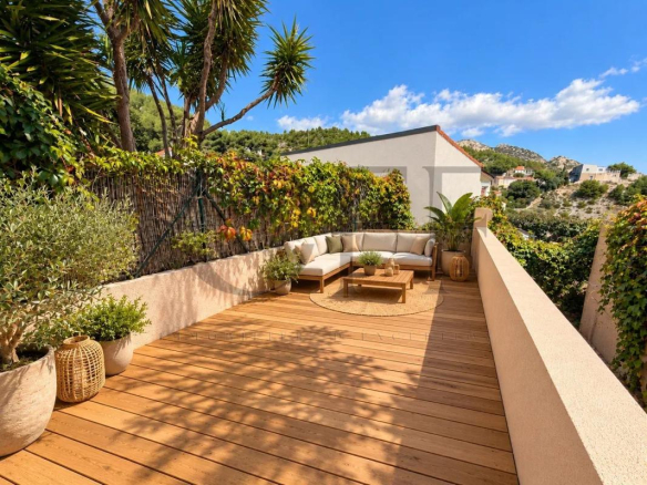Terrasse en bois avec mobilier de jardin, entourée de verdure, dans un cadre ensoleillé.