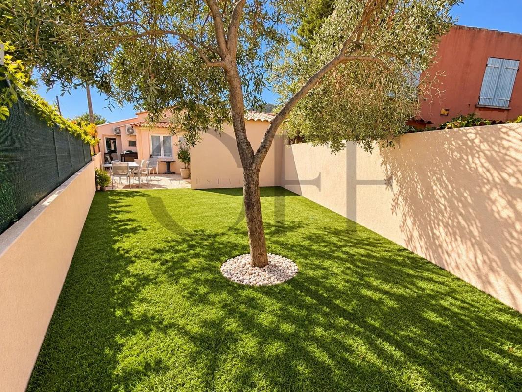 Maison de charme à Le Rove Jardin avec pelouse verte et un arbre au centre, maison en arrière-plan à Le Rove.