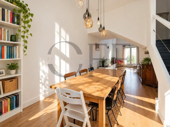 Salle à manger lumineuse avec une grande table en bois et des chaises, bibliothèque et décoration moderne.