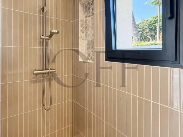 Douche moderne avec carrelage beige et fenêtre donnant sur l'extérieur.