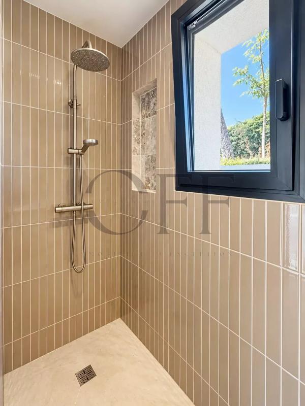 Douche moderne avec carrelage beige et fenêtre donnant sur l'extérieur.