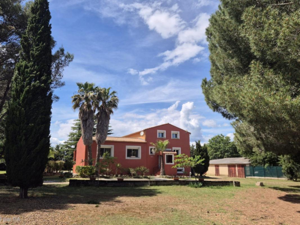 Maison rouge entourée d'arbres et d'un espace vert à Saint-Aunès.