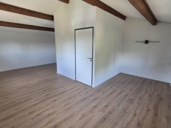 Intérieur d'une maison spacieuse avec un sol en bois et des poutres apparentes.